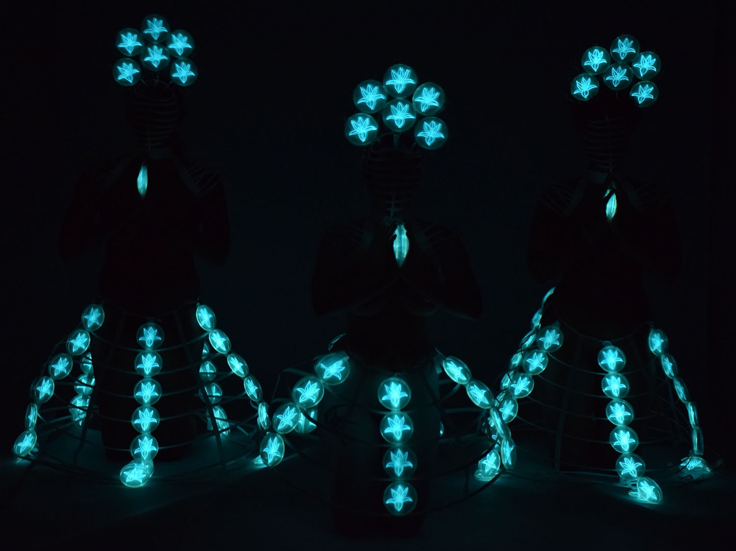 The Light of Prayer, figures illuminated by cyan bioluminescent forms in darkness